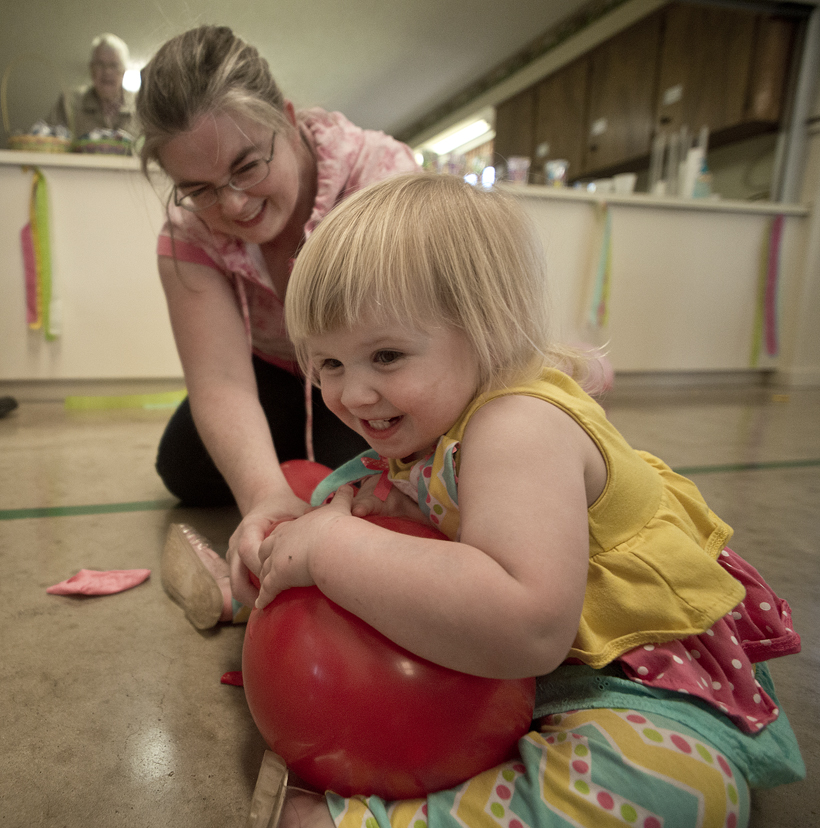 160326 WALBURG, TEXAS:  2-year-old Madeline De Reese of Jarrell, with her mom Kathleen De Reese,  works hard to pop a balloon  during Saturday's Easter Egg Hunt celebration at St. Peter Lutheran Church in Walburg.   After each year's Easter Egg Hunt, it's a tradition to go into the activity center and release even more energy by popping balloons before heading home.  Popping balloons was something little Madeline really enjoyed a lot!   Photo by Andy Sharp.